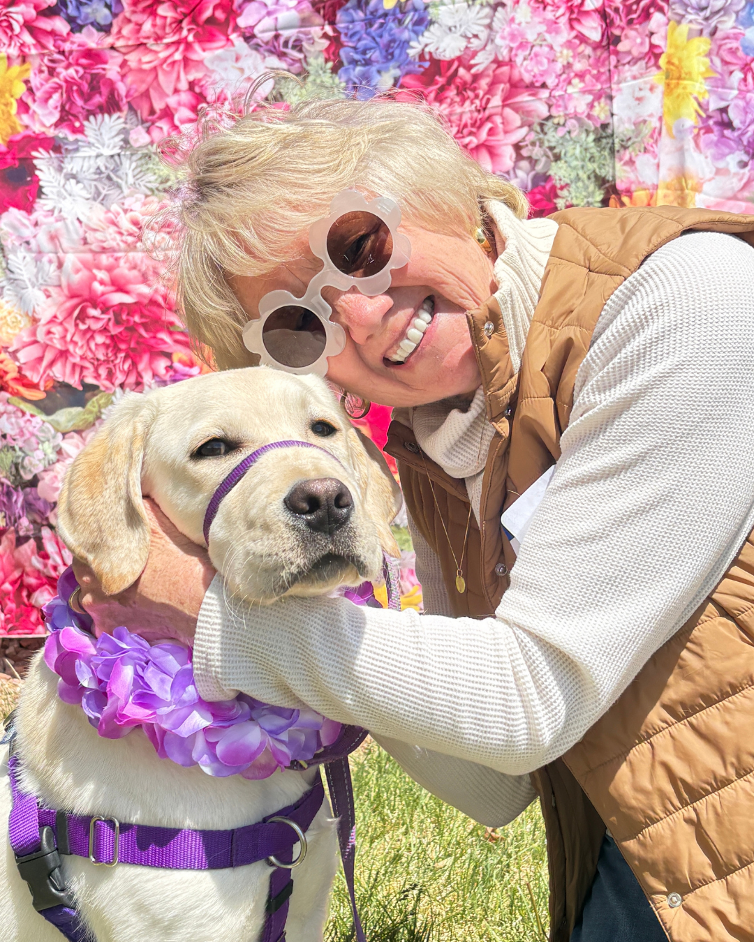 Lisa and Gilligan, a yellow lab, smile at the camera. Lisa has flower shaped sun classes.