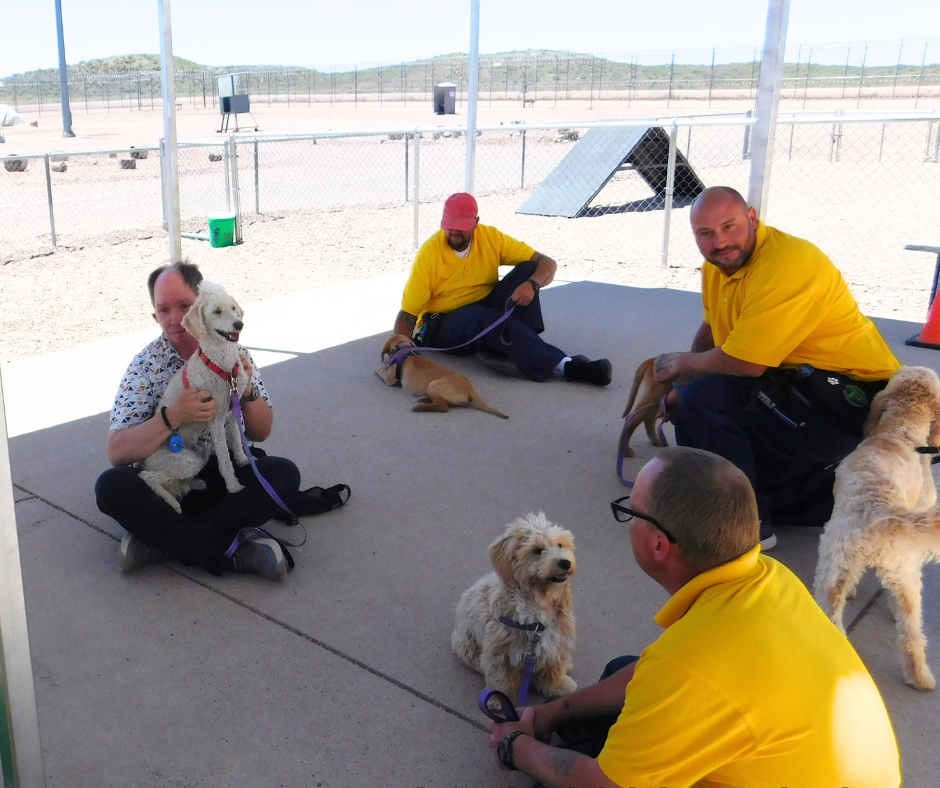 Harvey, Astro, and three inmates in yellow sit outside talking. Two other days hangout as they talk. 