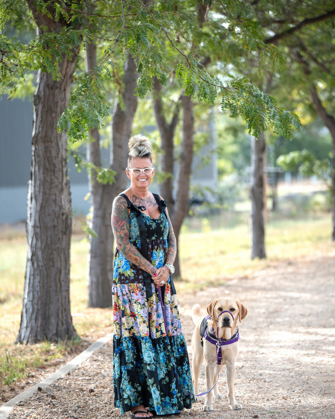 Melissa in a blue and green dress smiles at the camera. Next to her is Fortune, a yellow lab, looking at the camera intensely 