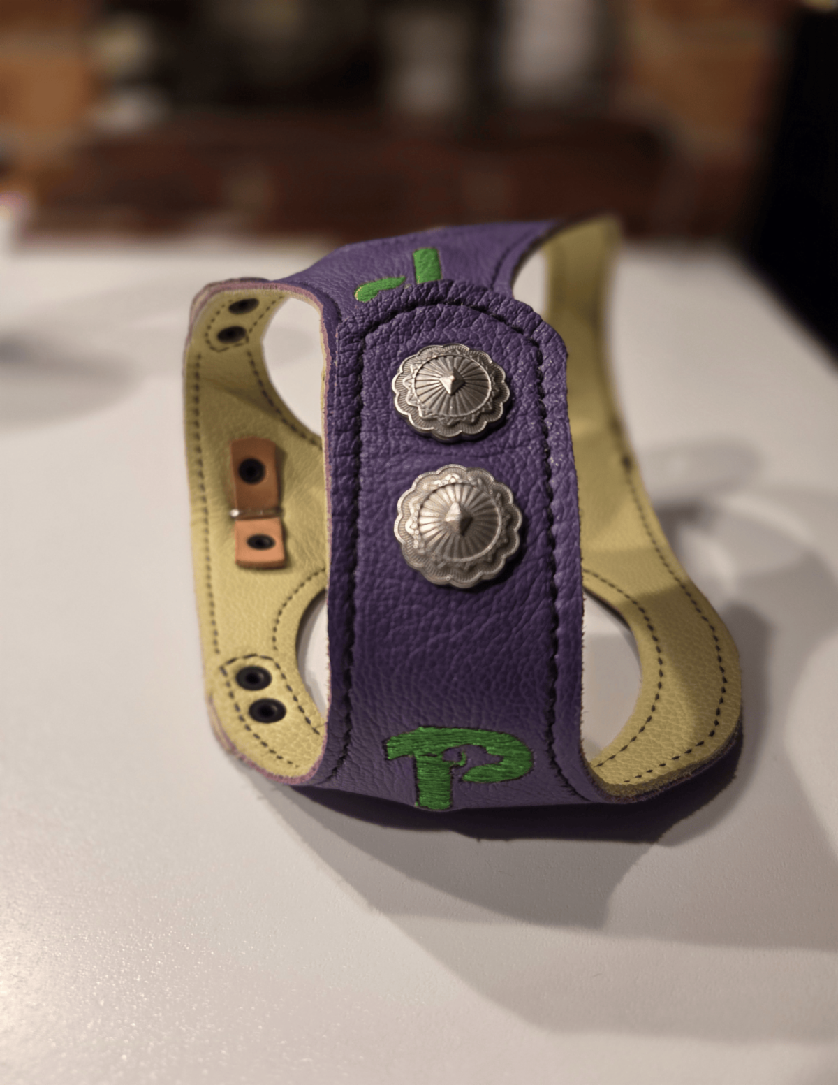 A purple leather harness with the Paragon logo on it sits on a bed. 