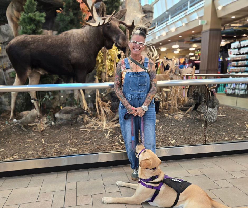 Melissa and Fortune, a yellow lab, pose in front of a taxidermy moose. He looks up at her lovingly. 
