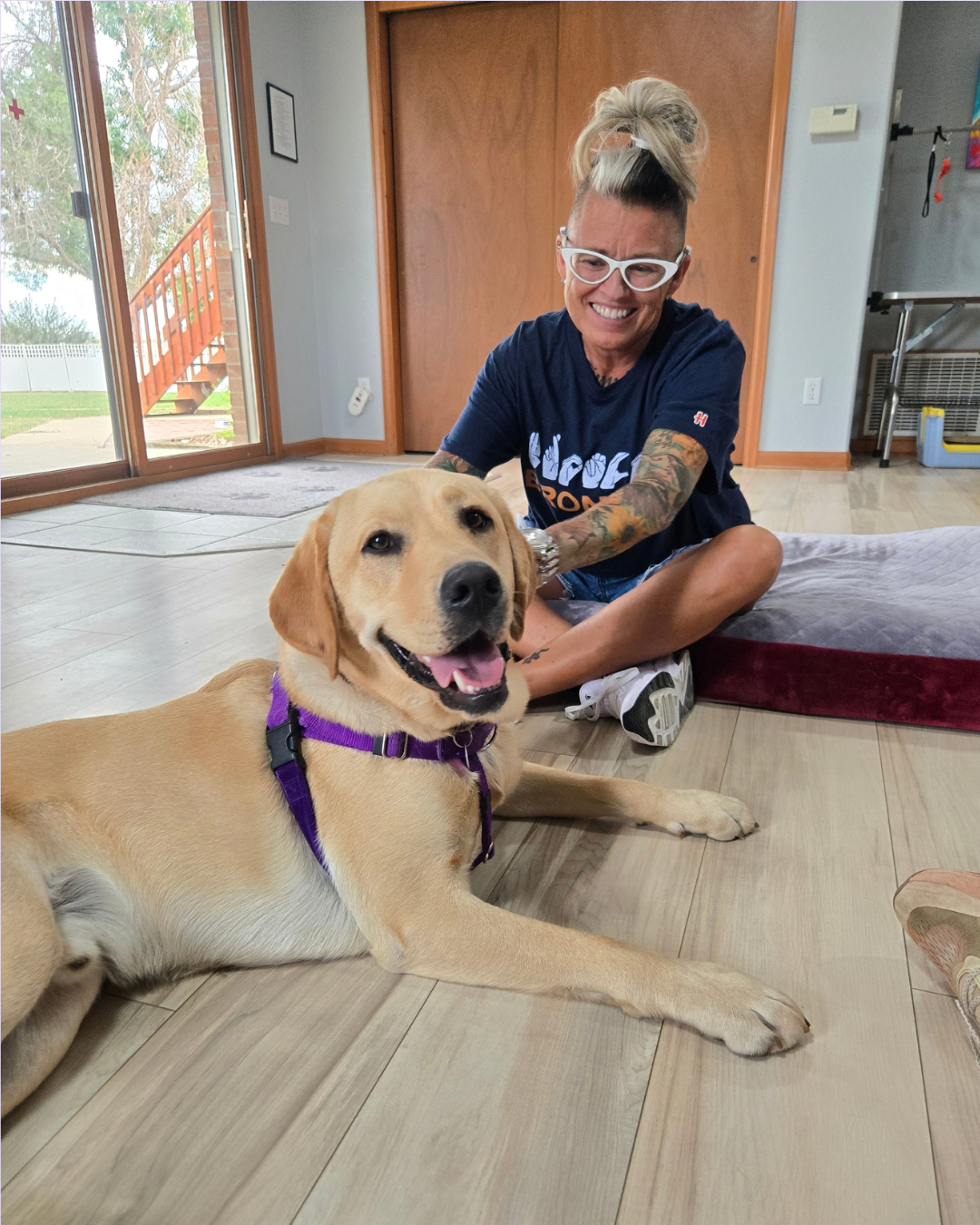Melissa beams while petting Fortune, a yellow lab. He looks at the camera smiling. 