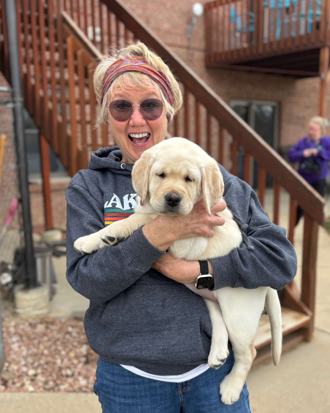 Gilligan's puppy raiser smiles while holding the 12 week old lab puppy. 