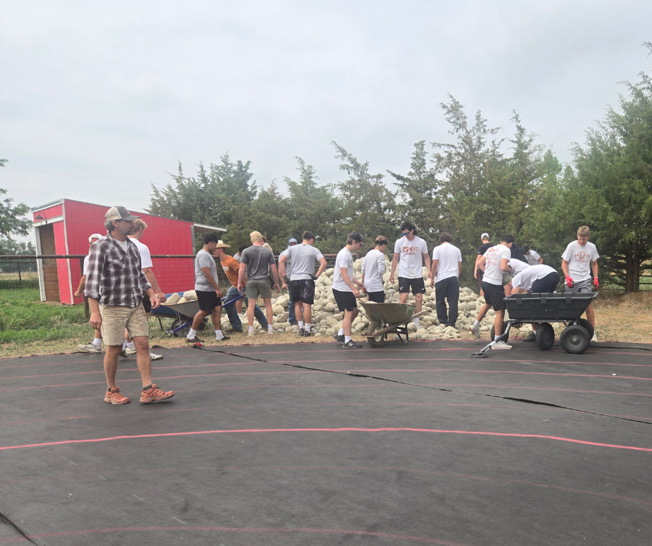 A group of high schoolers in white shirts move large river rocks.
