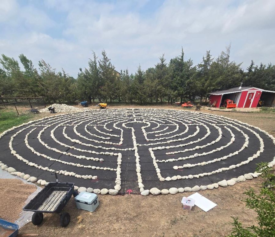 A black circle of weed cloth has stones creating a labyrinth pattern. 