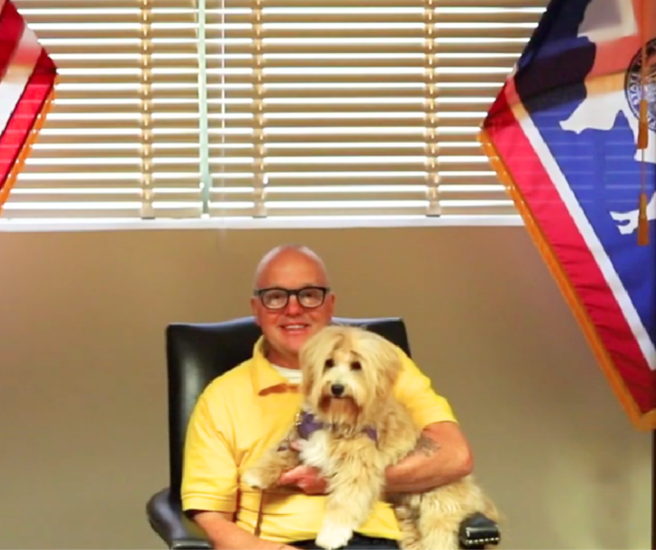 Master Inmate Handler Nic sits on a chair holding Finch a Havanese dog. 