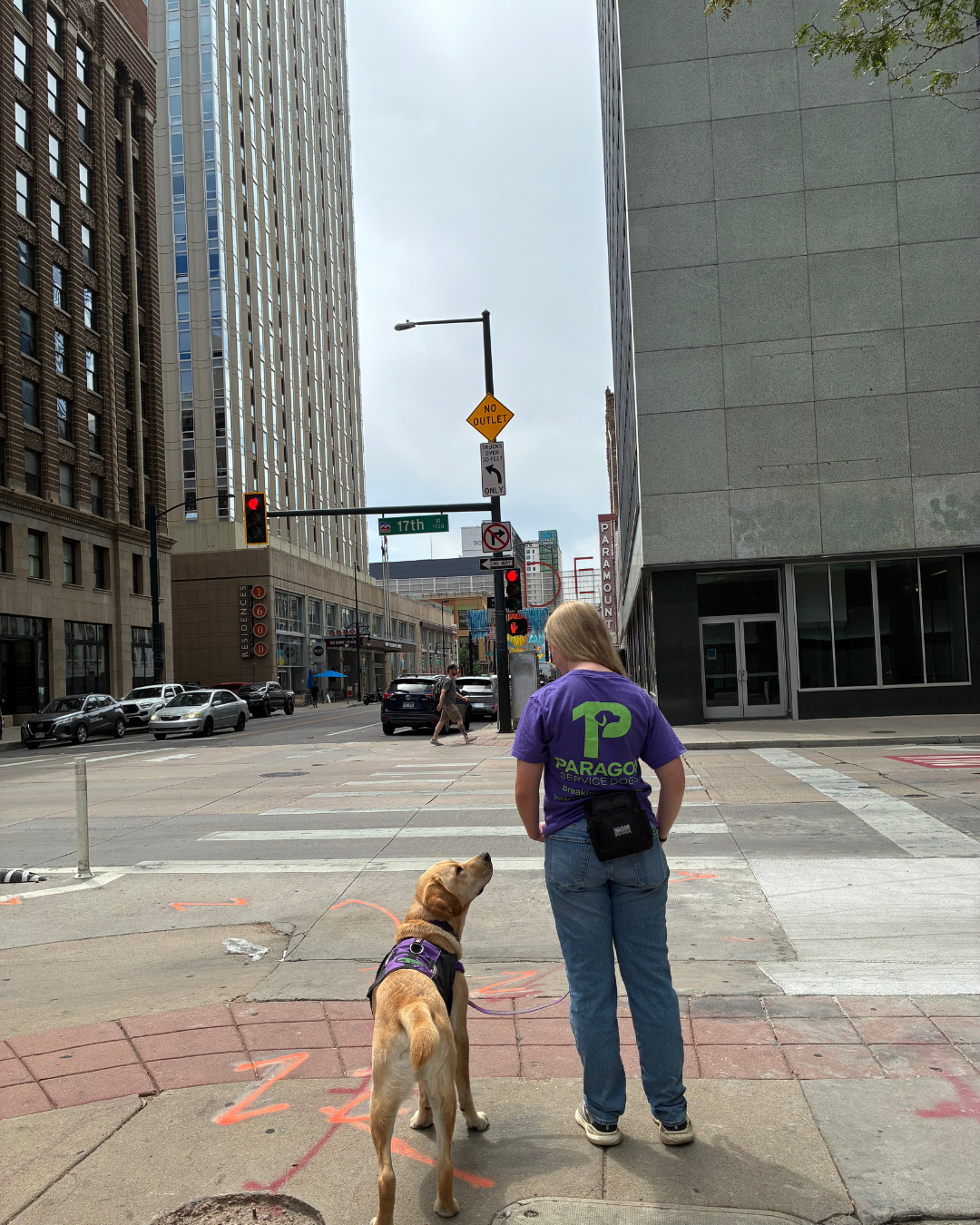 Staff member, Chloe stands smiling next to a yellow lab named Fortune in downtown Denver.