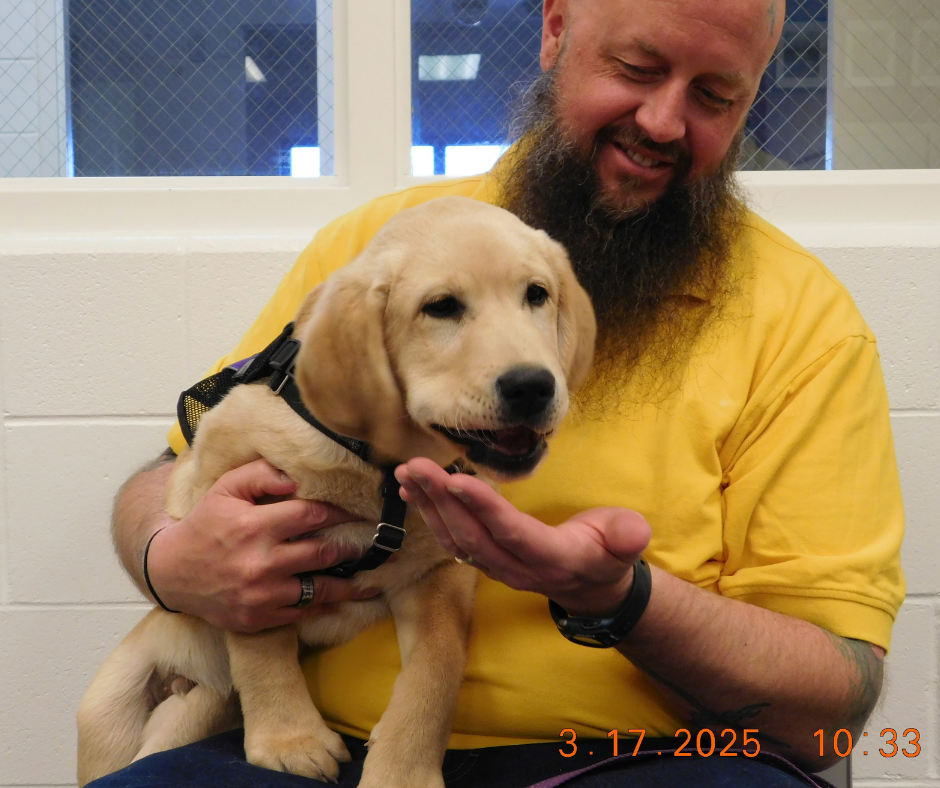 Chris, a inmate handler, carries Fortune. He puts his hand under Fortune's mouth to catch any treats he drops. 