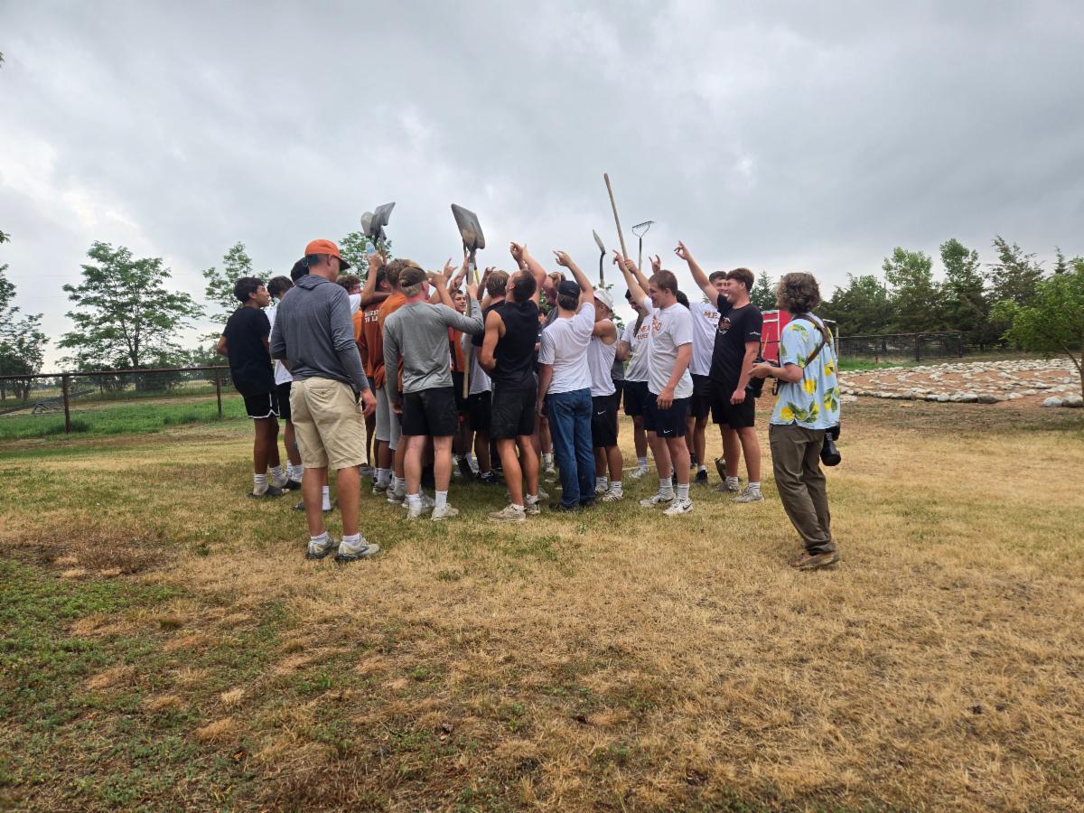 A large group of high schoolers gather raising the shovels in the air!
