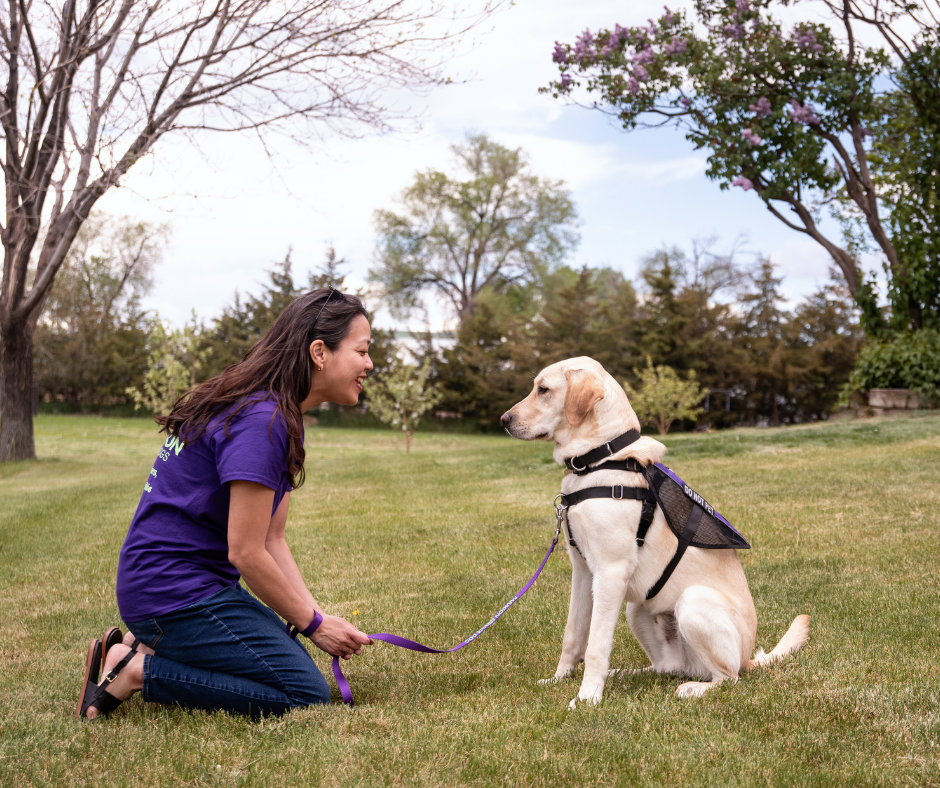 Vanessa sits smiling at a yellow lab. She's wearing a Paragon purple shirt. 