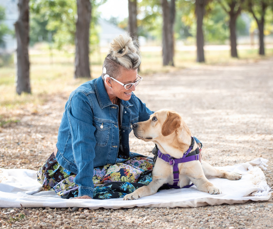 Melissa lays on a blanket with a demum jacket on. She is gazing into Fortune's, a yellow lab, eye as he lays next to her. 