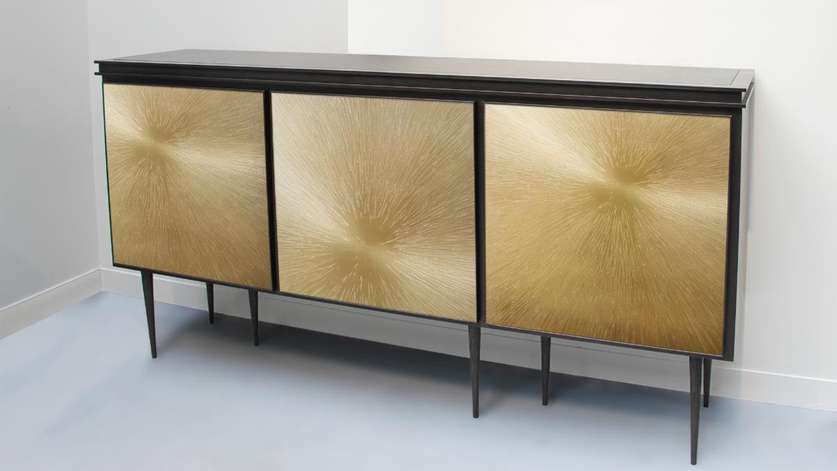 A sideboard with tall, thin legs and three square cabinets with a bronze textured facade on each.