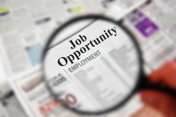 Magnifying glass over a newspaper headline that says Job Opportunity and employment