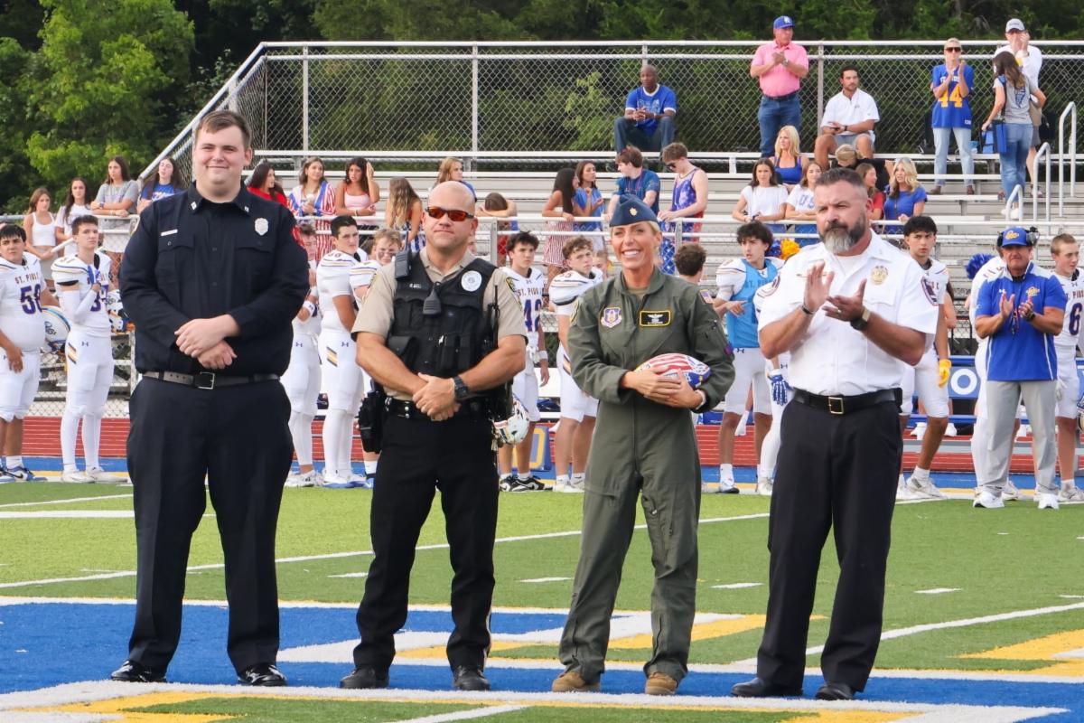 Four military and first responders posing for a photo on the football field with one of them holding the game ball.