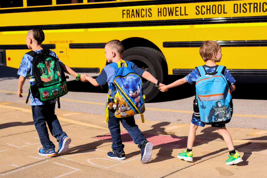 students hold hands while walking near a school bus
