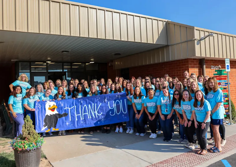 The staff at Henderson Elementary pose outside of the school with a large banner that reads "Thank you" after the community helped start the school year on time last year