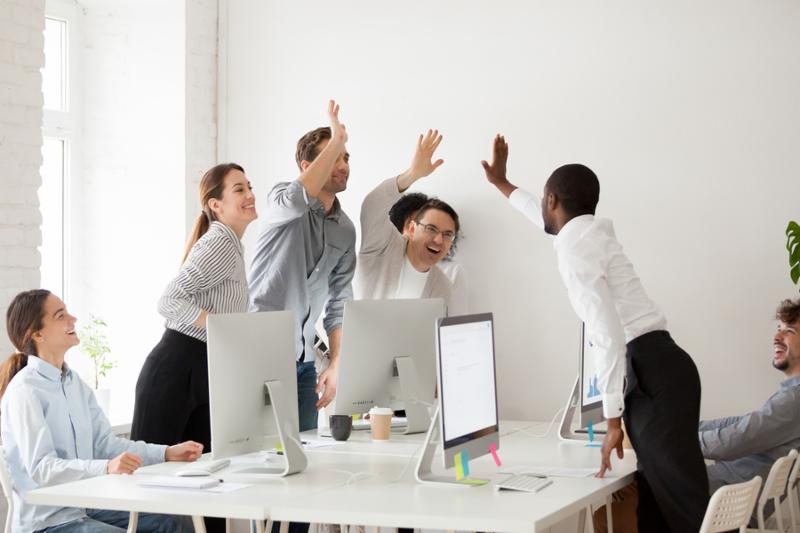 Happy multi-ethnic employees sales team giving high five together celebrating corporate success and good relations_ diverse group of office people joining hands excited by common victory achievement