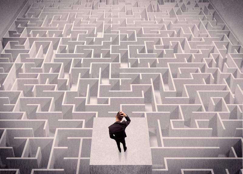 A confused businessman thinking while standing on a square platform above a detailed maze