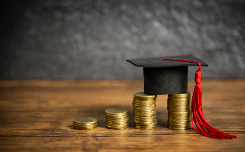Scholarships education concept with graduation cap on coin money saving  for grants education on wooden table dark background 