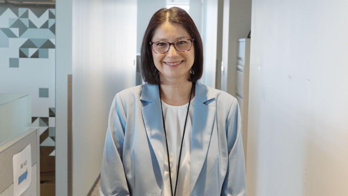 Jasmine Suo smiles at the camera in a building hallway wearing a blue blazer and white top