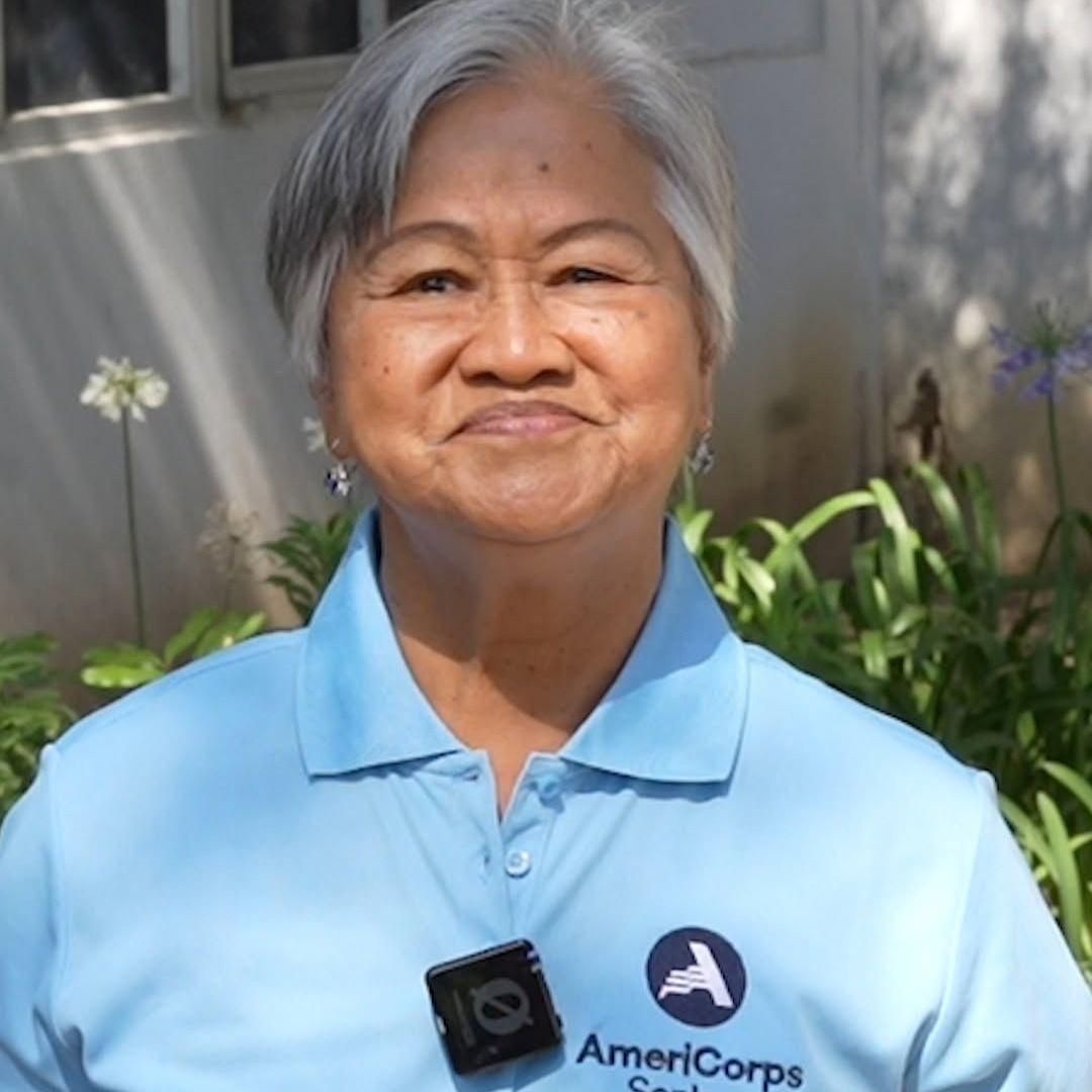 Virginia smiles at the camera wearing a light blue polo with the AmeriCorps logo on it