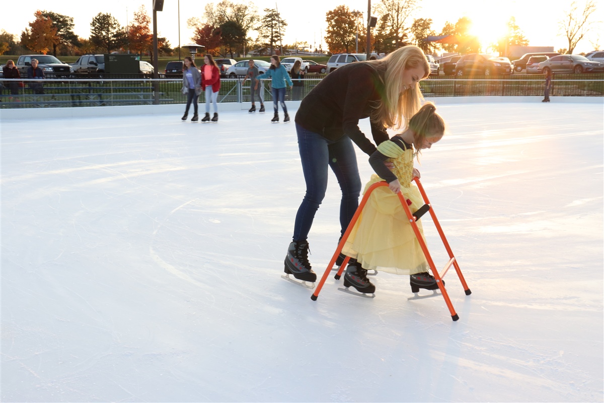 mom helping young daughter in a yellow princess dress ice skating outdoors