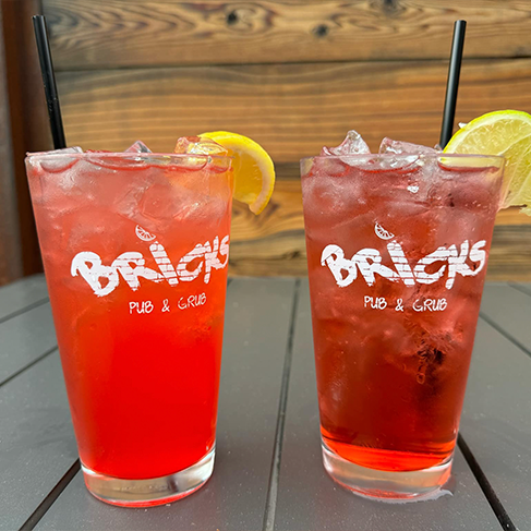two red drinks in clear cups on a table with the bricks restaurant logo on the cup