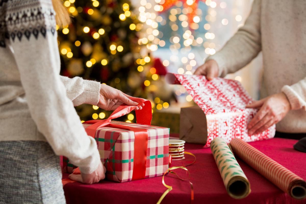 image of two people wrapping holiday gifts with holiday tree in background