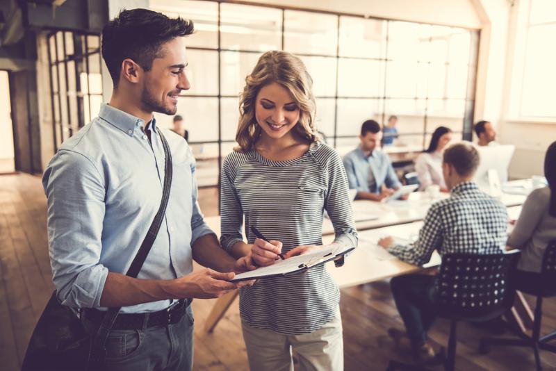 Handsome delivery man and beautiful business woman are talking and smiling in the background business people are working in office