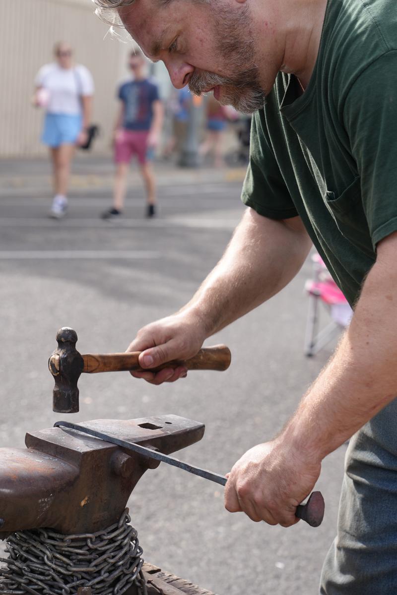 A metalworker strikes an in-progress piece against an anvil.