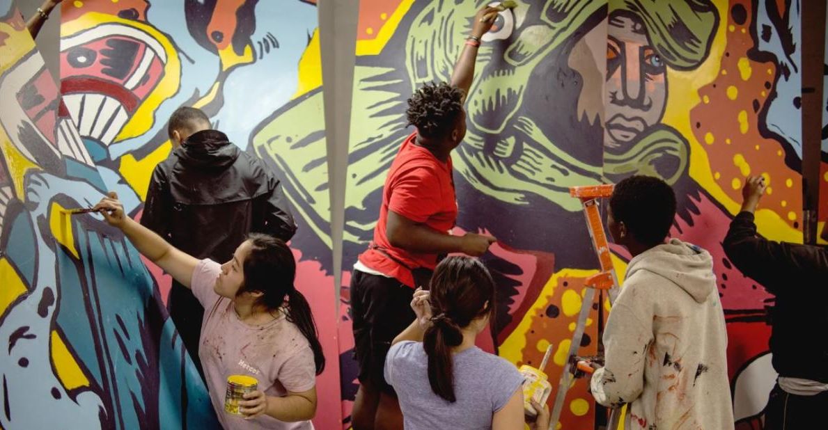 Photo showing a group of people collectively painting a mural. Urban ArtWorks is one of the Organization Award honorees at the 2023 Governor’s Arts & Heritage Awards. Photo courtesy of Urban ArtWorks.