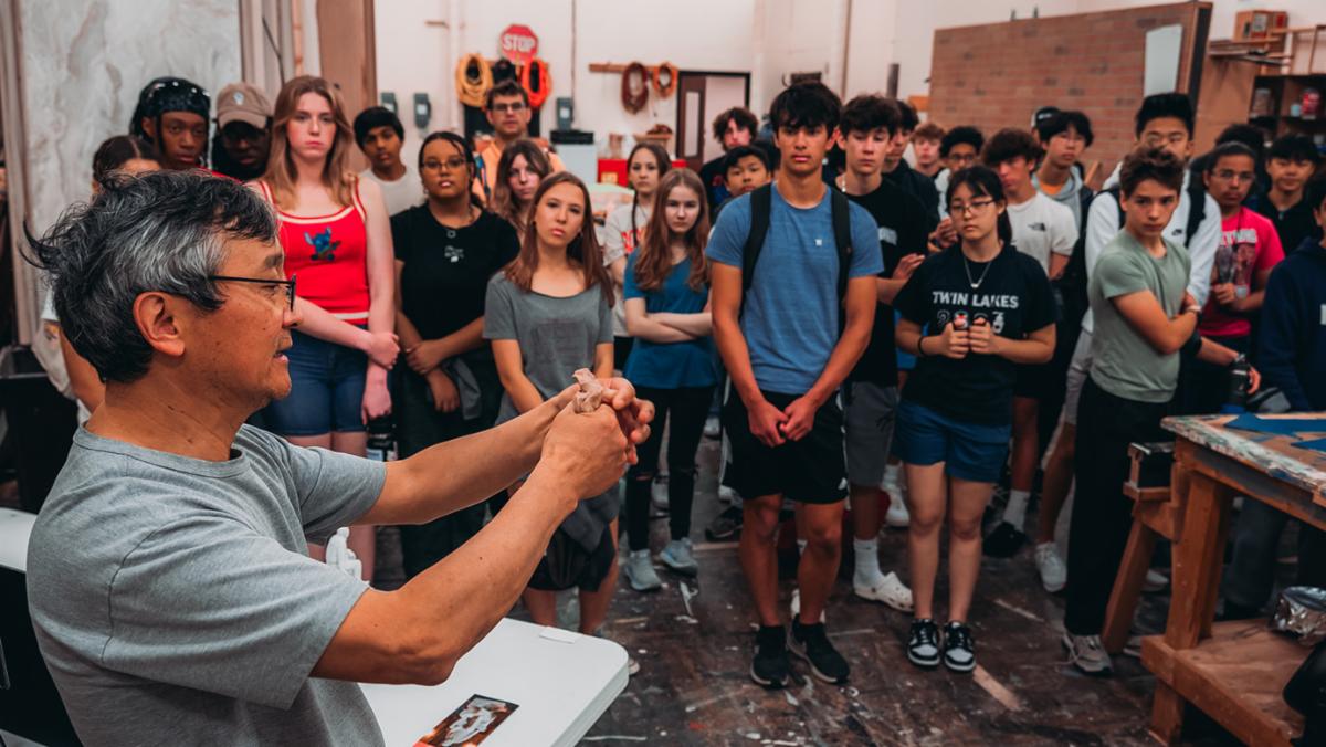 Artist Haiying Wu shows a group of students how he manipulates clay.