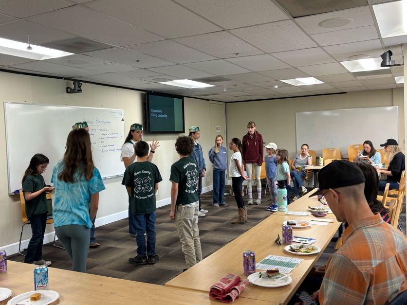 4-H county ambassadors and youth standing up in a classroom getting ready for an activity with parents sitting in tables around the group