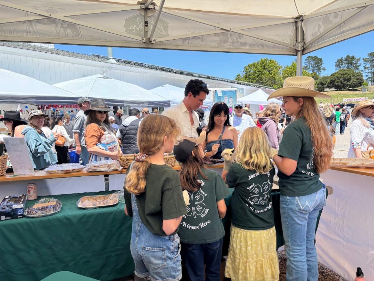 4-H members manning a bake sale booth with two interested customers. the members are wearing green Marin 4-H t-shirts with the 4-H clover. 