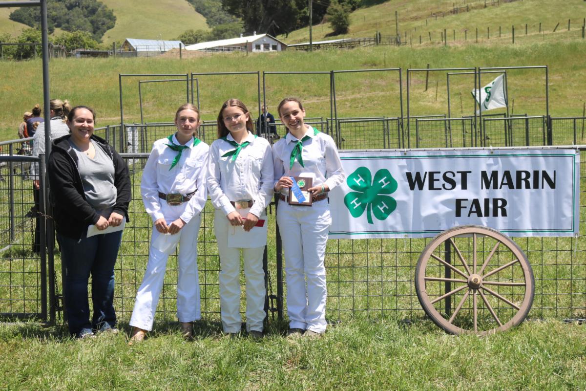 4 people posing in front of a "West Marin Fair" Sign
