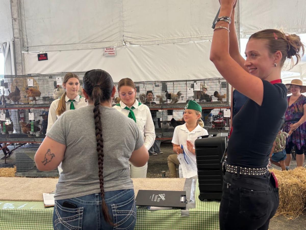 a group of youth talking to a small animal judge with guests and chicken cages in the background