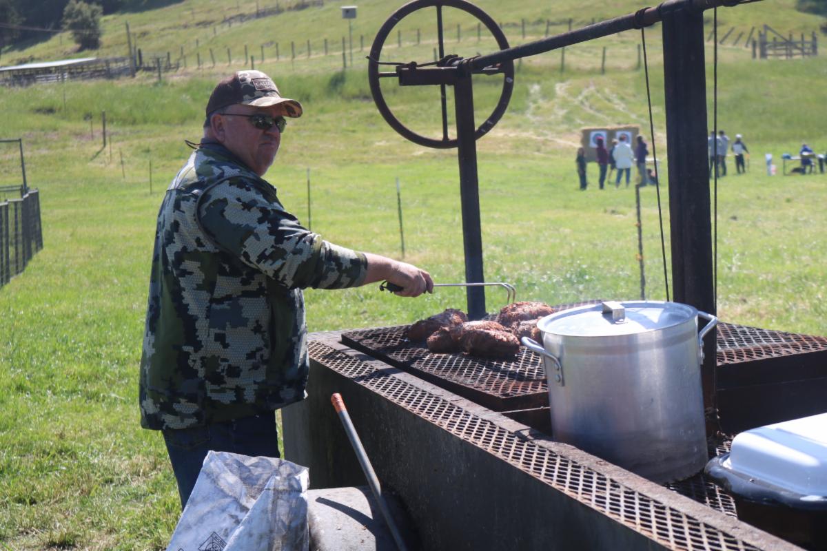 a man sitting at a large BBQ with a steak cooking