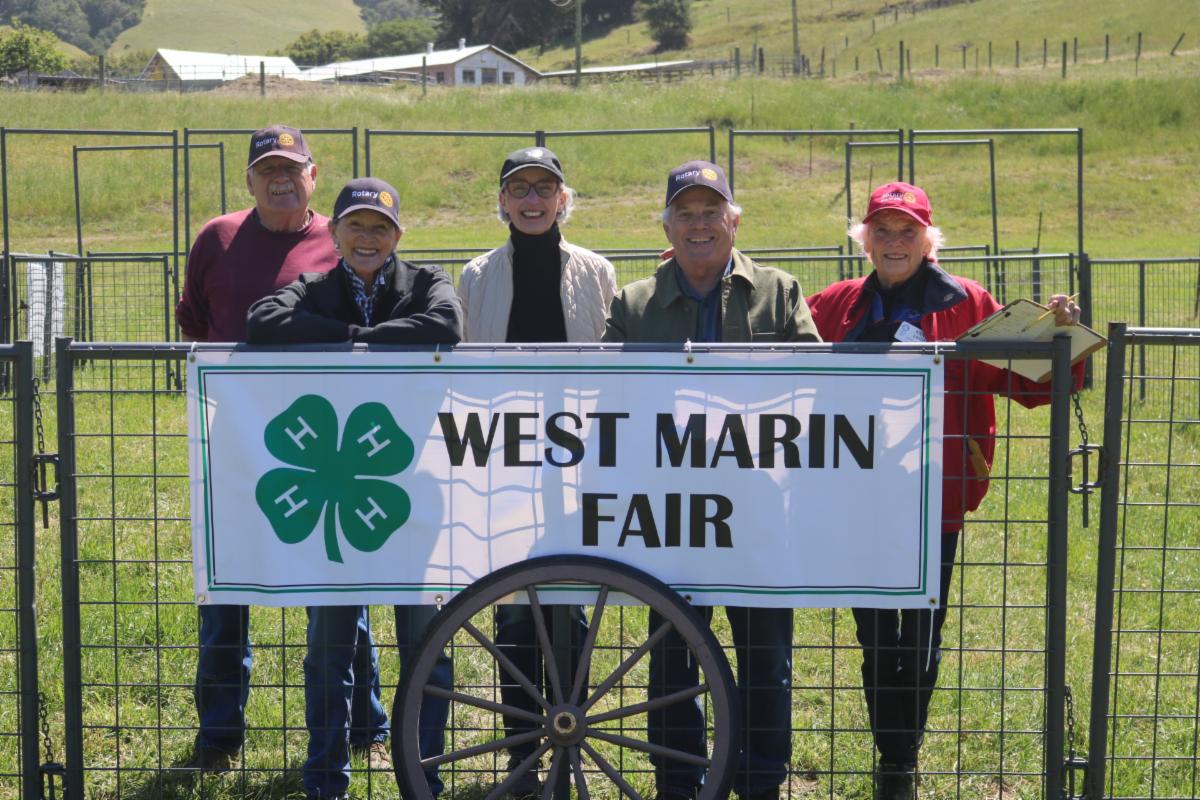5 people posing in front of a "West Marin Fair" Sign