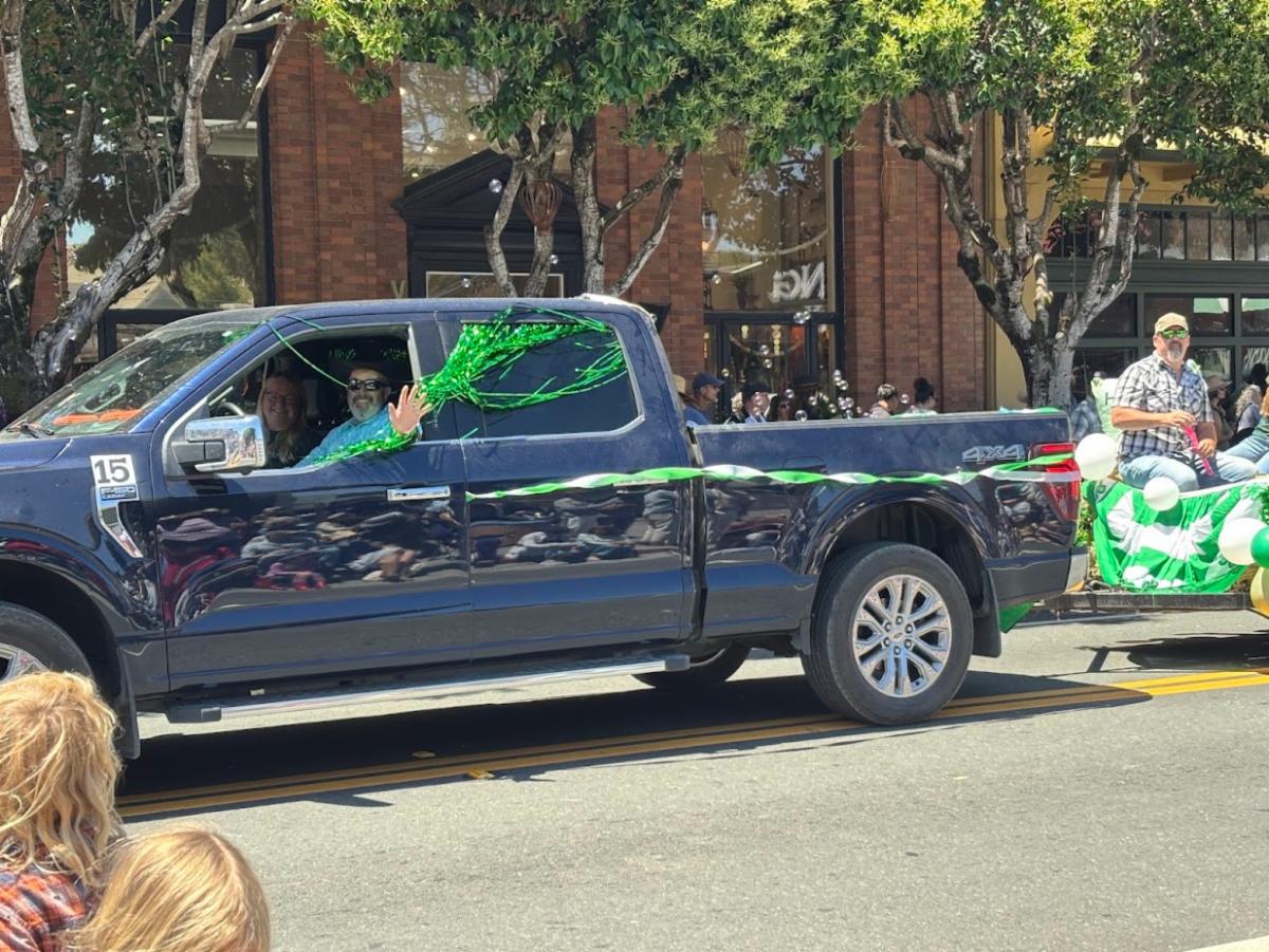 a blue truck with 2 people inside waving to the crowd in a parade
