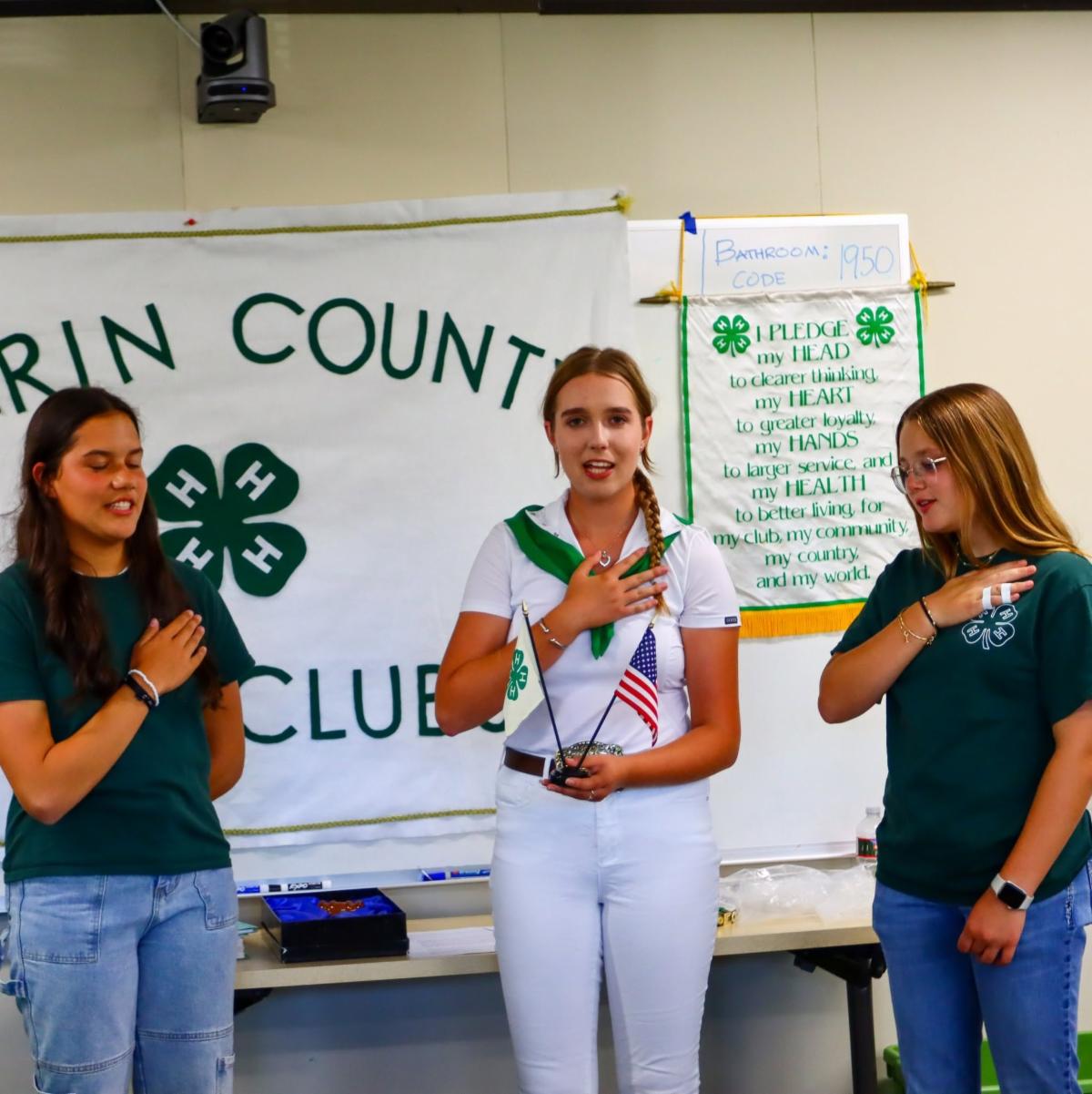 3 teen leaders demonstrating the 4-H pledge with a Marin County 4-H clubs banner and the 4-H pledge banner in the background.