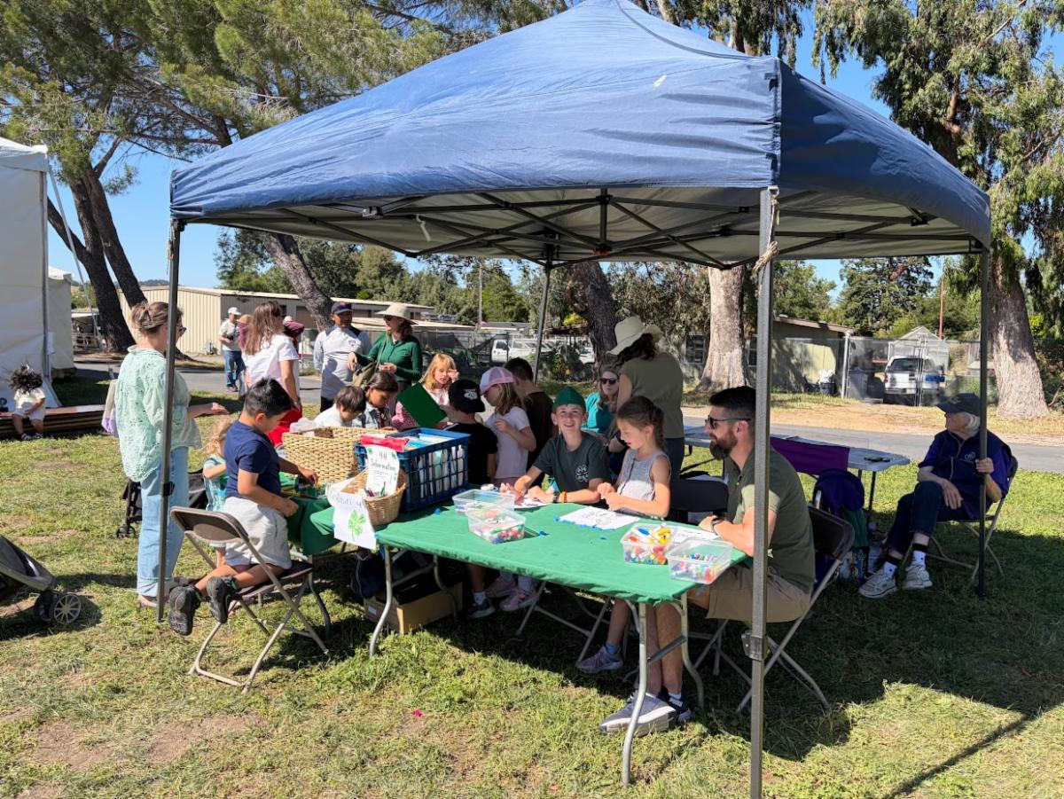 a group of 4-H members and families surrounding a 4-H booth with coloring and LEGO activities. 