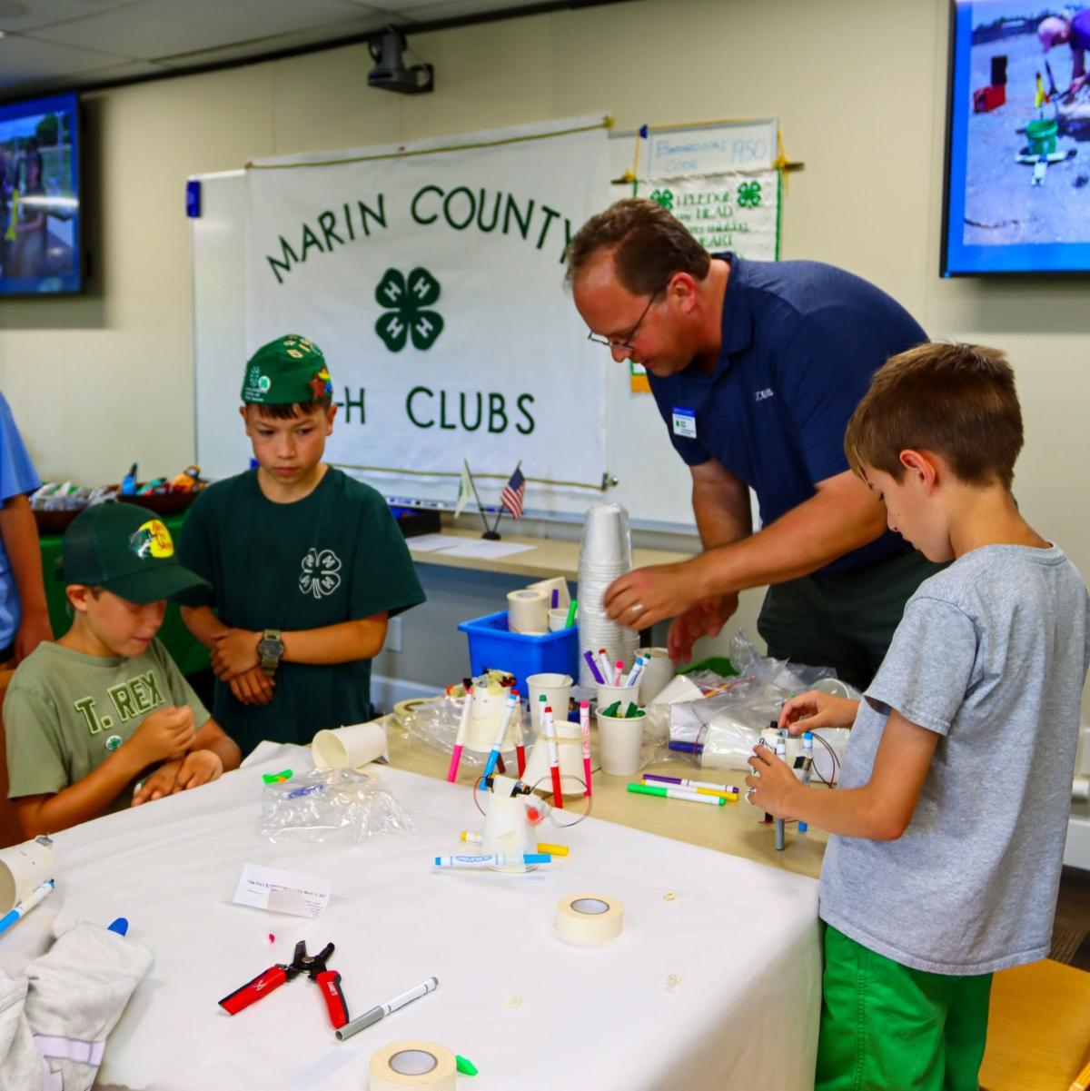 a group of 3 children and one adult with a hands on activity in front of them and a Marin County 4-H clubs banner in the background