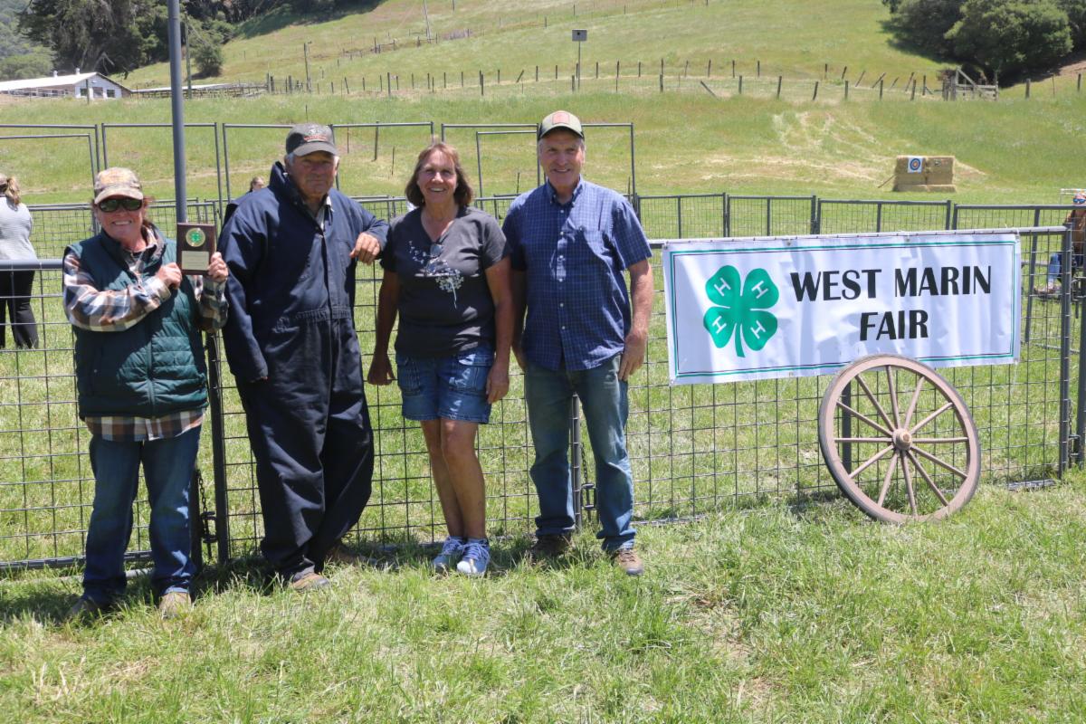 4 people posing in front of a "West Marin Fair" Sign