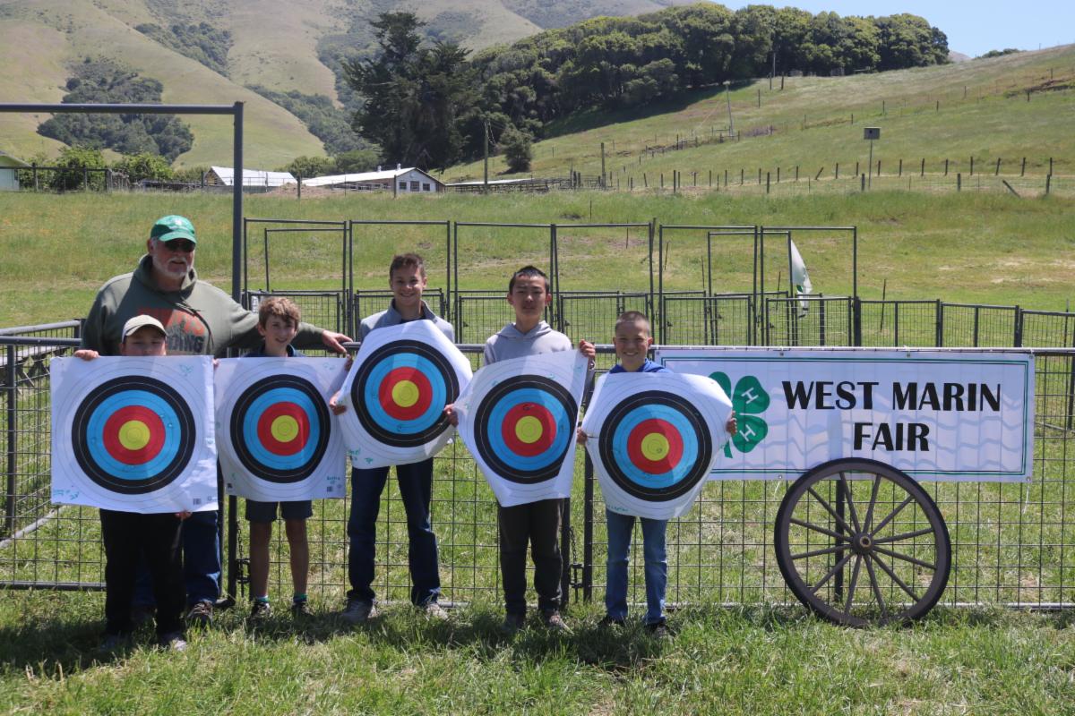 6 people posing in front of a "West Marin Fair" Sign