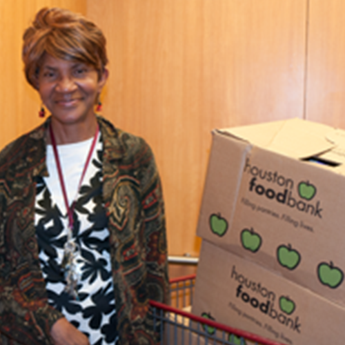 A senior woman smiles at the viewer while standing beside food bank boxes