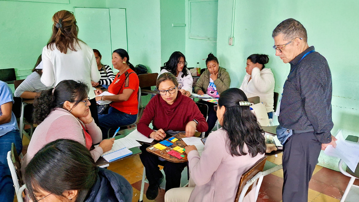 Teachers in a classroom work in small groups with colorful math manipulatives while a facilitator observes and offers guidance