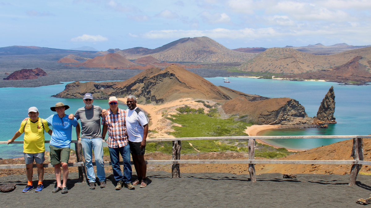 Five travelers stand at a scenic overlook on Bartolome Island in the Galapagos with turquoise bays and volcanic hills in the background