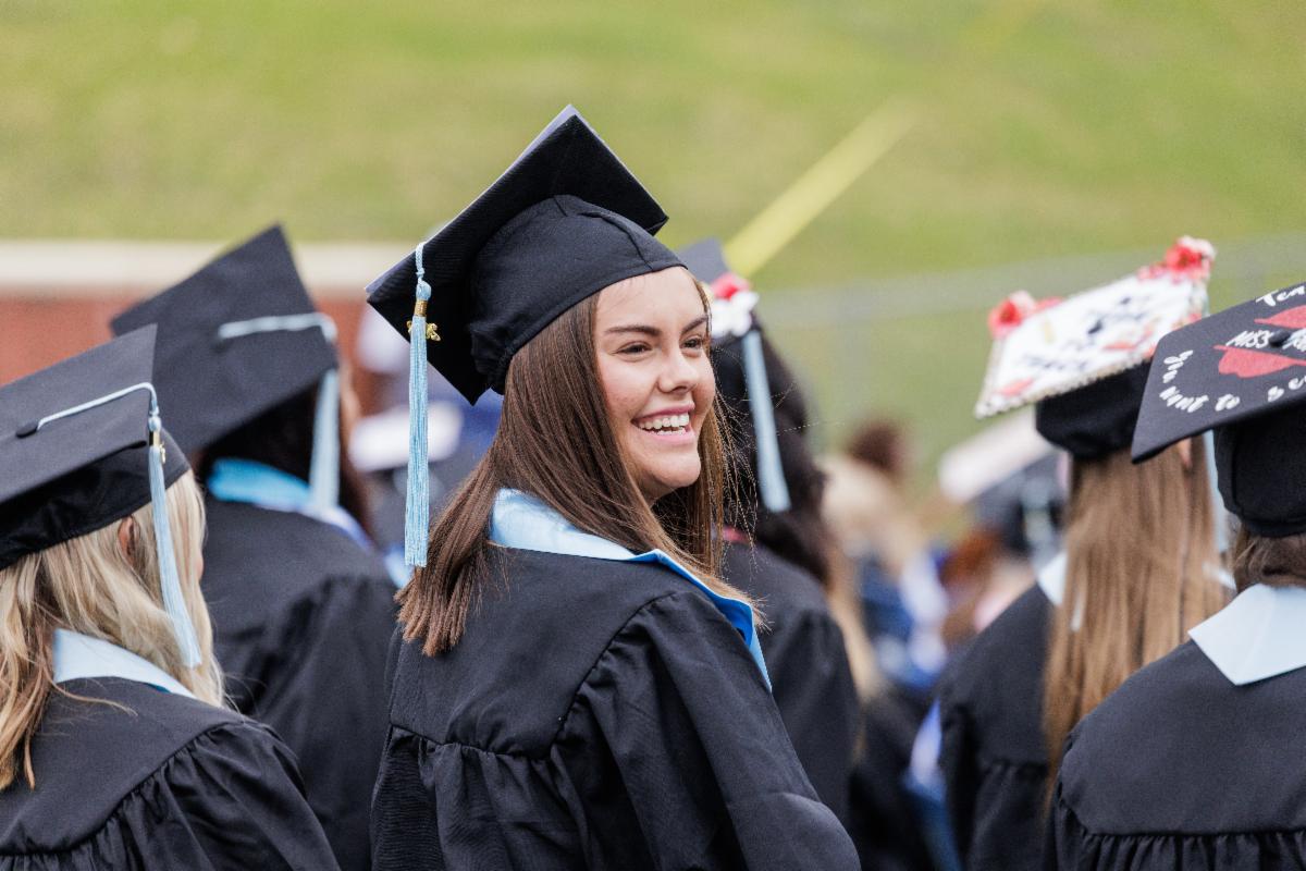 Photo of a girl in crowd of people  in gowns and mortar board hats as she turns with a smile