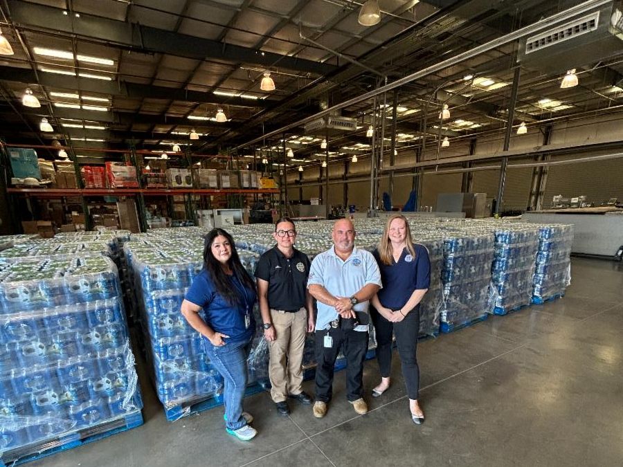 Individuals posing for a group photo next to palettes of bottled water in a warehouse