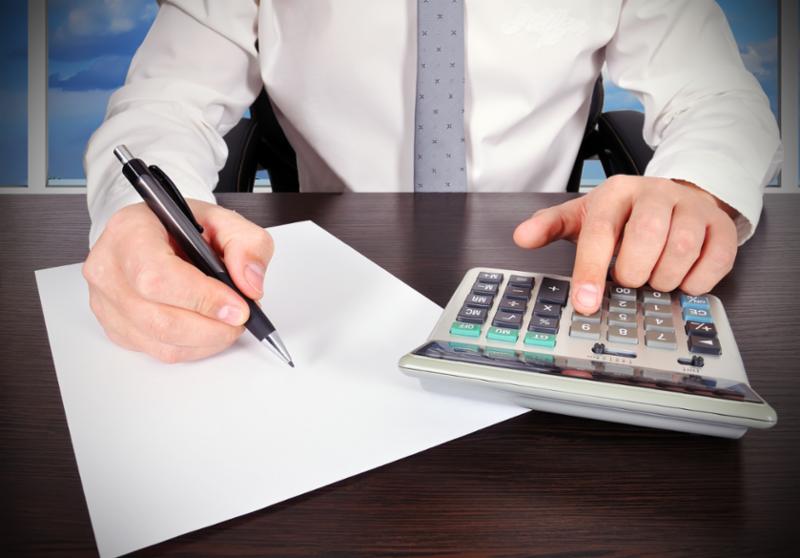 Stock photo of a man with a calculator writing figures on a note pad.